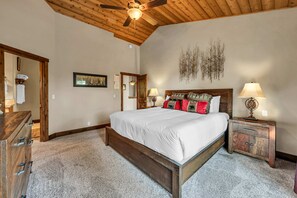 A bedroom with a wooden ceiling, a bed with white bedding, two bedside tables with lamps, a wooden dresser, and a wall-mounted artwork. - Tahoe City Retreat | Lake View & Hot Tub (Tahoe City)