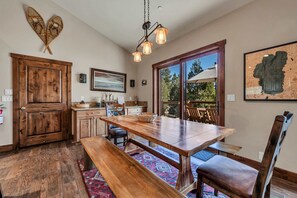 A spacious kitchen with a wooden table and benches, a large window with a view of trees, and a rustic wooden door. - Tahoe City Retreat | Lake View & Hot Tub (Tahoe City)