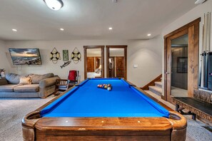 A pool table in a room with a couch, a painting, and a door leading to another room. - Tahoe City Retreat | Lake View & Hot Tub (Tahoe City)