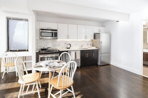 A modern kitchen with white cabinetry, stainless steel appliances, and a dining area with wooden chairs. - Large UES 1BD Balcony Rooftop Gym (New York)