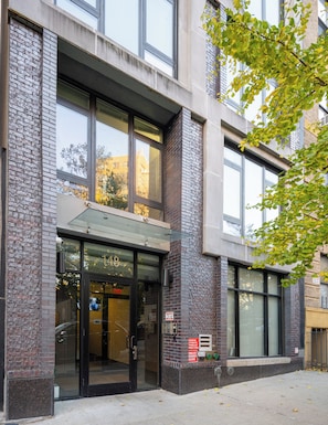 A building with a glass entrance, a brick facade, and a number '148' displayed above the door. - Large UES 1BD Balcony Rooftop Gym (New York)
