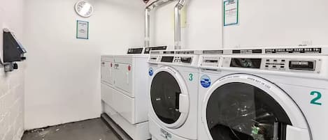 A laundry facility with two front-loading washers and a dryer, numbered 2 and 3, with control panels and a clock on the wall.