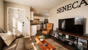 Una sala de estar con sofá, mesa de centro, televisor y una cocina al fondo.