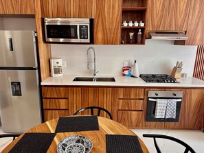 A modern kitchen with wooden cabinets, stainless steel appliances, and a dining area with a patterned table. - Luxury & Modern Penthouse in the Heart of Zona Romántica - Walk Everywhere! (Puerto Vallarta)