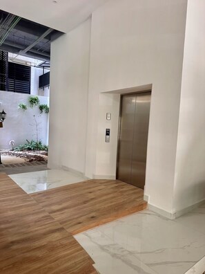 A modern interior with a wooden floor, a white wall, and a metallic elevator. - Luxury & Modern Penthouse in the Heart of Zona Romántica - Walk Everywhere! (Puerto Vallarta)