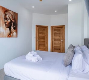 A bedroom with a bed, pillows, a painting, and wooden doors. - Villa Orchid 3BR Seaview villa with private pool (Chaweng)