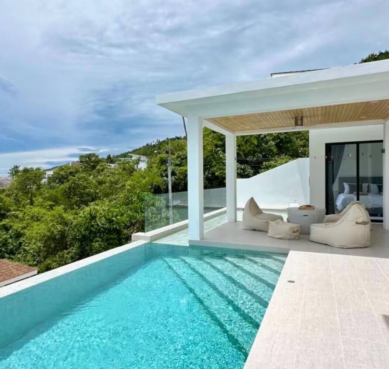 Un área de piscina moderna al aire libre, con vistas despejadas de la vegetación circundante y un espacio de estar techado.