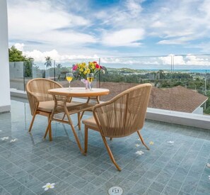 Ein Balkon mit Korbstühlen, einem kleinen runden Tisch und einem Blumenstrauß.