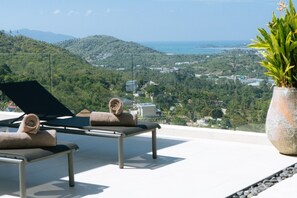 A terrace with two lounge chairs, a potted plant, and a view of a coastal landscape. - Luxury 6-Bedroom Villa with Sea View and Gym (Chaweng)