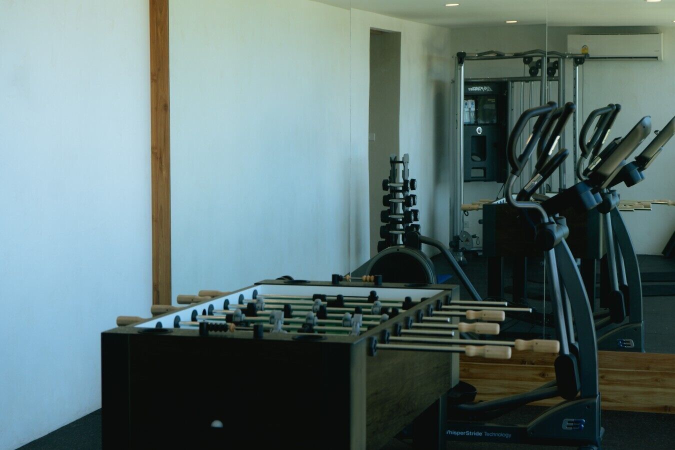 A gym with exercise equipment including a foosball table, treadmills, and weight machines.