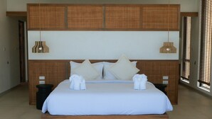 Ein Hotelzimmer mit einem großen Bett, zwei Nachttischen, einem Kopfteil mit gewobenen Paneelen und einem Fenster mit Jalousien.