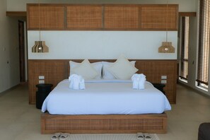A hotel room with a large bed, two bedside tables, a headboard with woven panels, and a window with blinds. - Luxury 6-Bedroom Villa with Sea View and Gym (Chaweng)