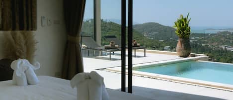 Habitación de hotel con una cama grande, vista a una piscina y un paisaje pintoresco.