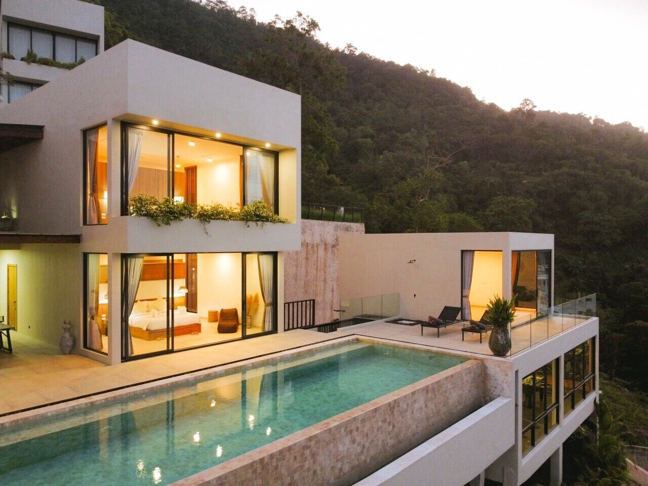 Una casa moderna de dos pisos con piscina, ventanas amplias y un balcón.