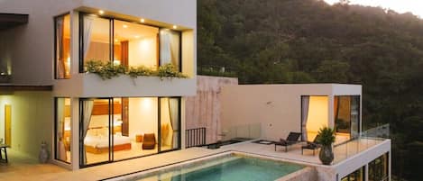 Una casa moderna de dos pisos con piscina, ventanas amplias y un balcón.