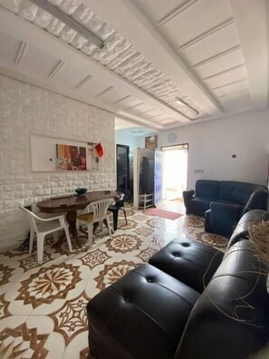 Una sala de estar con piso estampado, un sofá de cuero negro, una zona de comedor con mesa y sillas, y una pared de ladrillo blanco.