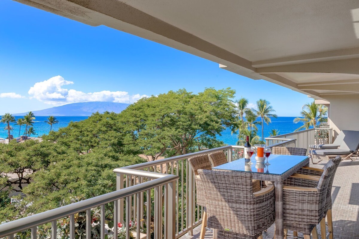 Ein Balkon mit Korbmöbeln, einem Tisch und Blick auf das Meer und die Berge.