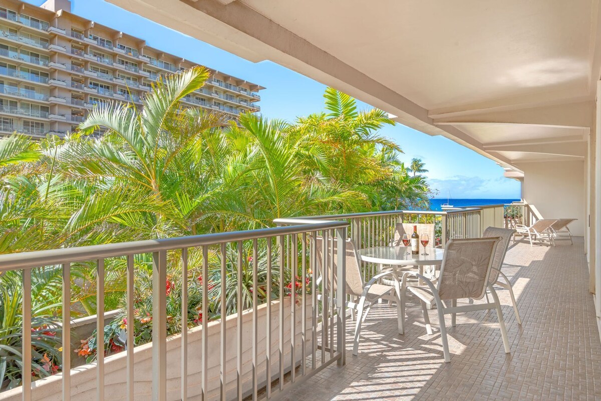 Ein Balkon mit Tisch und Stühlen, der auf ein Gebäude und den Blick aufs Meer blickt.