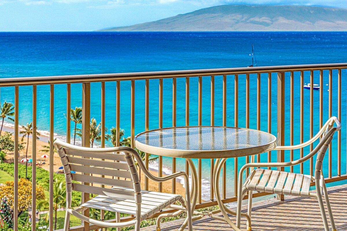 Ein Balkon mit rundem Tisch und zwei Stühlen, mit Blick auf einen Strand und den Ozean.