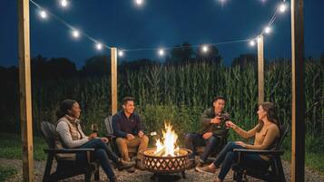 A group of people sitting around a fire pit with string lights overhead in an outdoor setting.