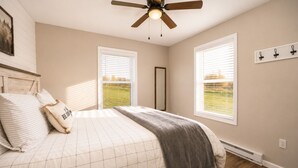 A bedroom with a bed, a ceiling fan, and two windows with blinds.