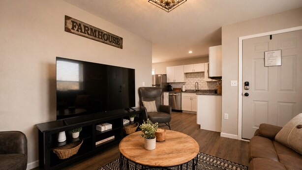 A living room with a television, a sofa, a coffee table, and a kitchen in the background.