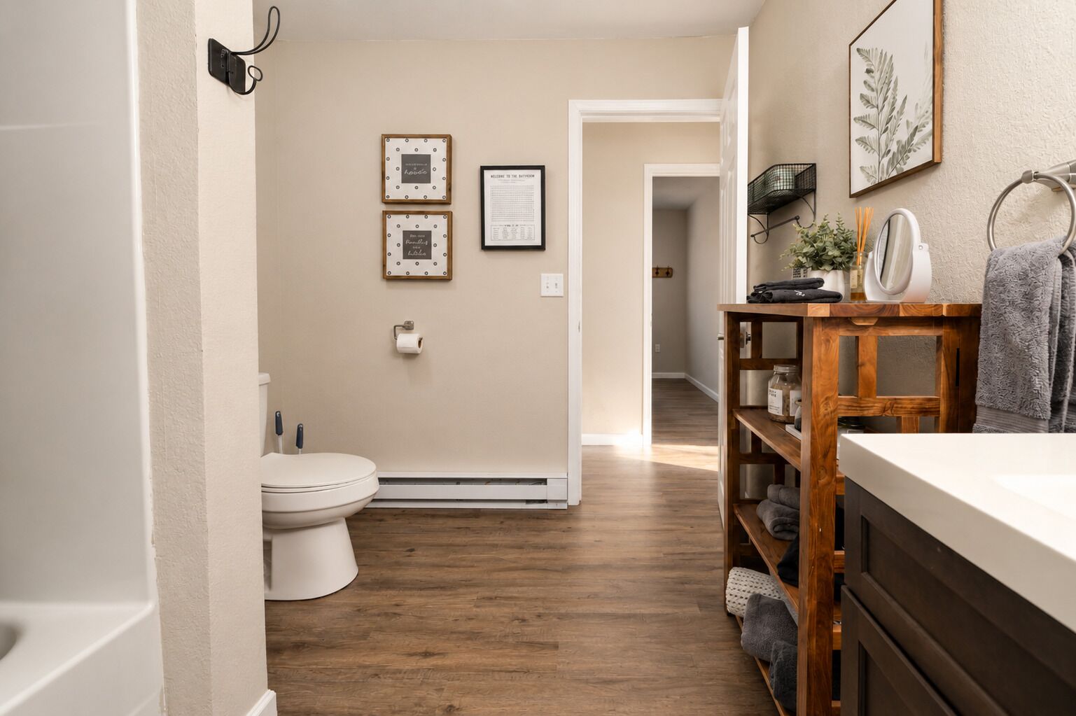 Une salle de bain avec des toilettes, un plancher en bois, un lavabo blanc et une étagère contenant des articles de toilette.
