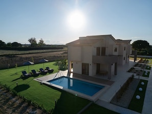 A modern two-story house with a swimming pool, a lawn, and a view of the countryside.
