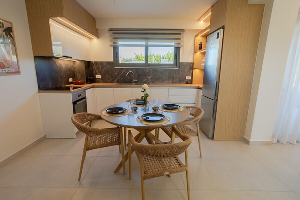 A modern kitchen with a dining area, featuring a round table with chairs, a built-in oven, and a window with a view.
