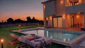 Ein modernes Haus mit Schwimmbad, Sitzgelegenheiten im Freien und einer gut beleuchteten Terrasse.