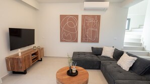 Ein modernes Wohnzimmer mit einem Flachbildfernseher, einer Holz-Unterhaltungseinrichtung, einem grauen Ecksofa und zwei abstrakten Wandbildern.