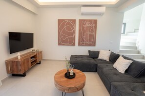 A modern living room with a flat-screen TV, a wooden entertainment unit, a grey sectional sofa, and two abstract wall art pieces.