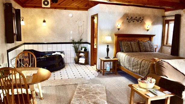 Una habitación acogedora con una cama, una silla, una mesa, una mesita de noche con una lámpara y un calentador de pared.