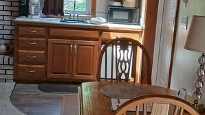 Cocina compacta con muebles de madera, microondas y lavamanos. Hay una mesa de comedor con sillas.
