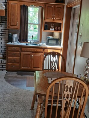 A compact kitchen with wooden cabinets, a microwave, and a sink. There is a dining table with chairs. - Romantic Queen Cottage with Jacuzzi & Fireplace (Berlin)