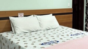 A hotel room with a bed, a wooden headboard, a patterned bedspread, and a pink blanket. - Hotel Opção (Manaus)