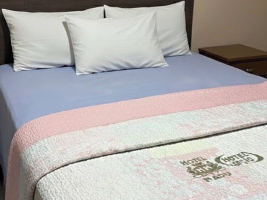 Una cama con almohadas blancas y una colcha azul, una mesita de noche y una pared con una puerta.