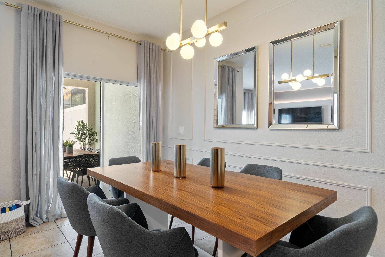 A modern dining area with a wooden table, grey upholstered chairs, and pendant lighting.