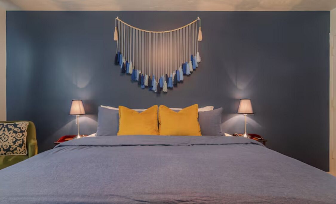 Una cama con una colcha gris, dos almohadas amarillas y dos lámparas de noche.