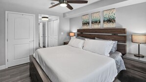 Ein Schlafzimmer mit Bett, Deckenventilator, Nachttisch, Lampe und einer Tür.