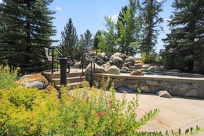 A landscaped outdoor area with a stone wall, a small waterfall, and a metal staircase leading to a seating area. - First Tracks at Wildhorse | Gondola + Hot Tubs (Steamboat Springs)