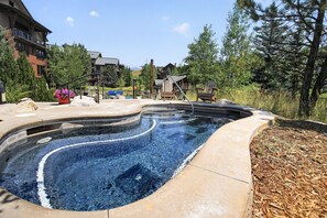 A hot tub with a curved design, surrounded by a wooden deck and a landscaped area with trees and shrubs. - First Tracks at Wildhorse | Gondola + Hot Tubs (Steamboat Springs)