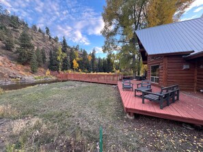 Une cabane en rondins dotée d’une terrasse, de meubles de jardin et offrant une vue sur la rivière.