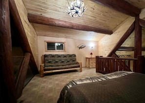 A wooden loft bedroom with a bed, a bench, a dresser, and a window.