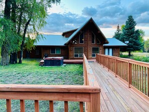 Une cabane en rondins dotée d’une terrasse, entourée d’arbres et bordée d’une pelouse.