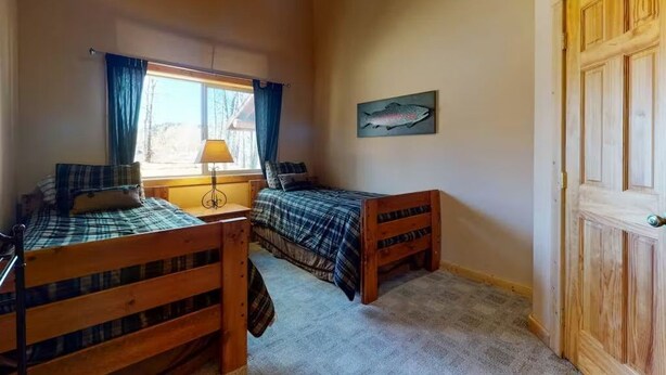Een kamer met twee houten bedden, een raam met gordijnen, een lamp en een schilderij van een vis aan de muur.