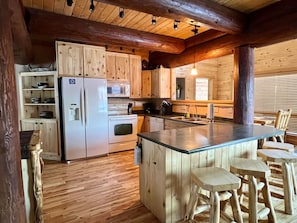 L’intérieur d’un chalet en bois comprend un coin cuisine équipé d’un réfrigérateur, d’une cuisinière et de tabourets de bar en bois.