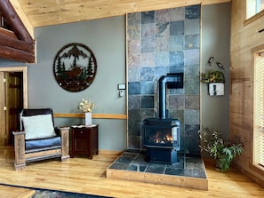 A cozy room with a stone fireplace, a wooden bench, a small table with a vase, and a wall-mounted heater.