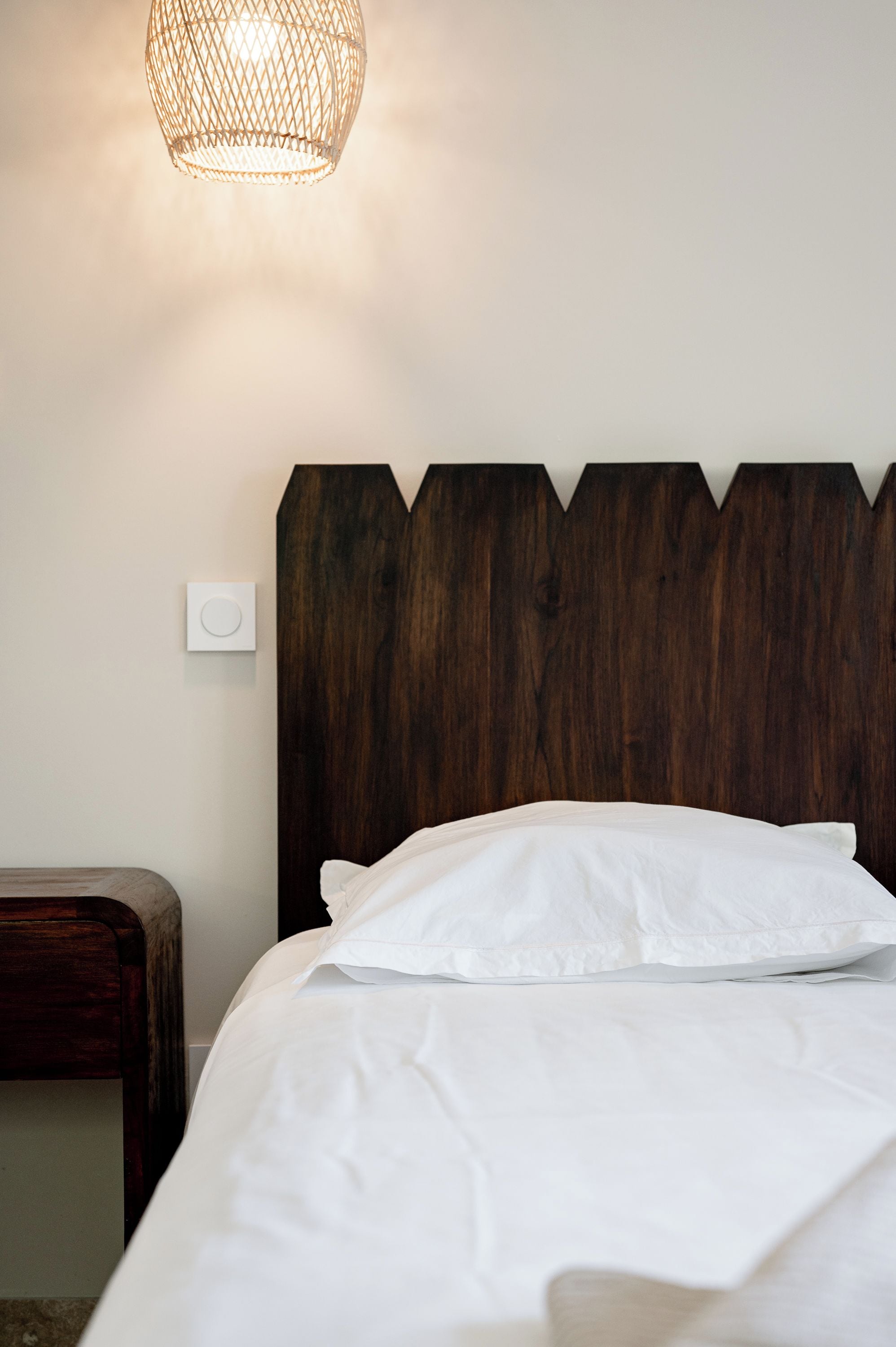 A bed with a wooden headboard, white bedding, and a hanging light fixture.