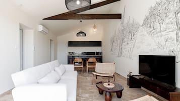 Uma sala de estar moderna com um sofá branco, uma mesa de jantar de madeira com cadeiras, uma TV e uma parede com um mural em preto e branco.
